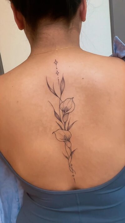 Fine line lily spine tattoo running down the center of the back.