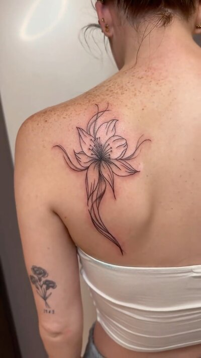 Fine line lily tattoo with smoky abstract shading on a shoulder blade.