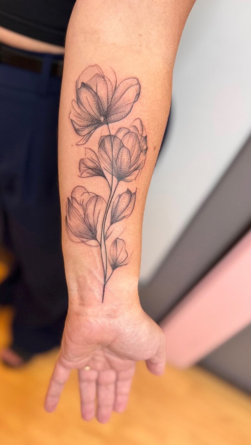 Wispy fine line magnolia tattoo on a forearm.