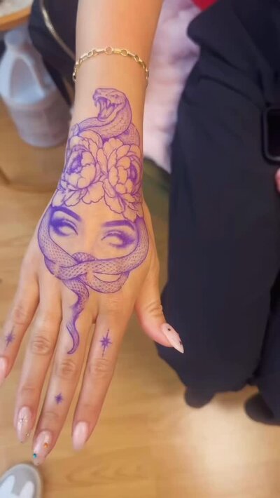 Medusa and snake fine line tattoo across the back of a hand, freshly done.